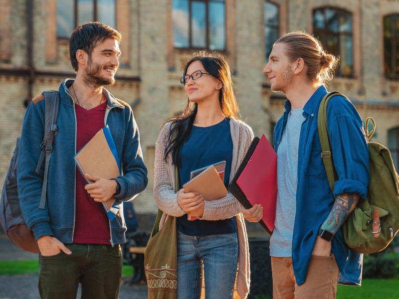 3 students walking on campus holding books smiling