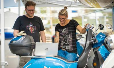 Two people look ta a laptop on a electronic scooter