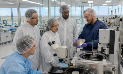 Semiconductor technicians and apprentices examine a silicon wafer with an instructor in a modern electronics manufacturing training lab.