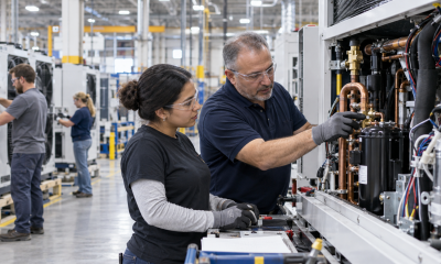 Manufacturing employees inspect copper tubing and mechanical components while assembling industrial cooling equipment on a modern factory floor.