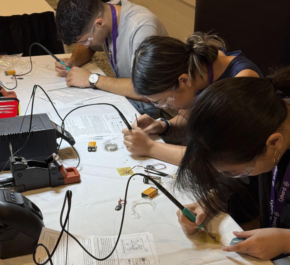 A group of 3 students working on soldering circuit boards
