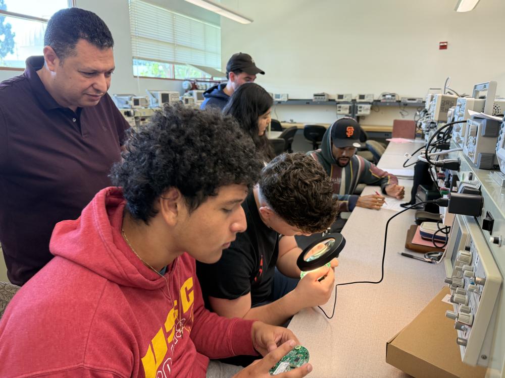 Students looking at circuit boards through a magnifying glass
